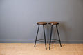 Two wooden stools with black metal legs against a gray wall.