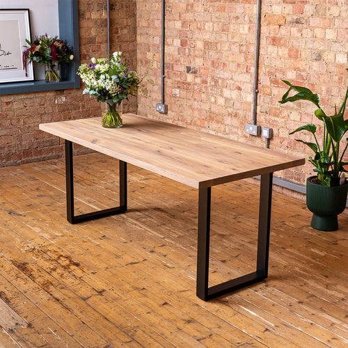 Wooden dining table with black metal legs in a room with brick walls and wooden floor.